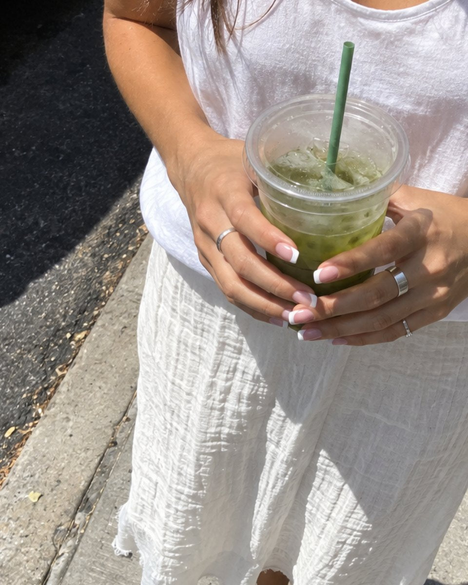 A white french tip manicure in daylight, hands holding an iced matcha